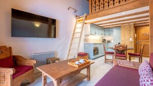 A cozy room with a wooden table, a sofa, a wooden ladder, a kitchen area, and a TV mounted on the wall. - Apt central proche des Pistes + Parking & Pool (Chamonix-Mont-Blanc)