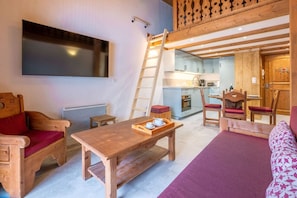 A cozy room with a wooden table, a sofa, a wooden ladder, a kitchen area, and a TV mounted on the wall. - Apt central proche des Pistes + Parking (Chamonix-Mont-Blanc)