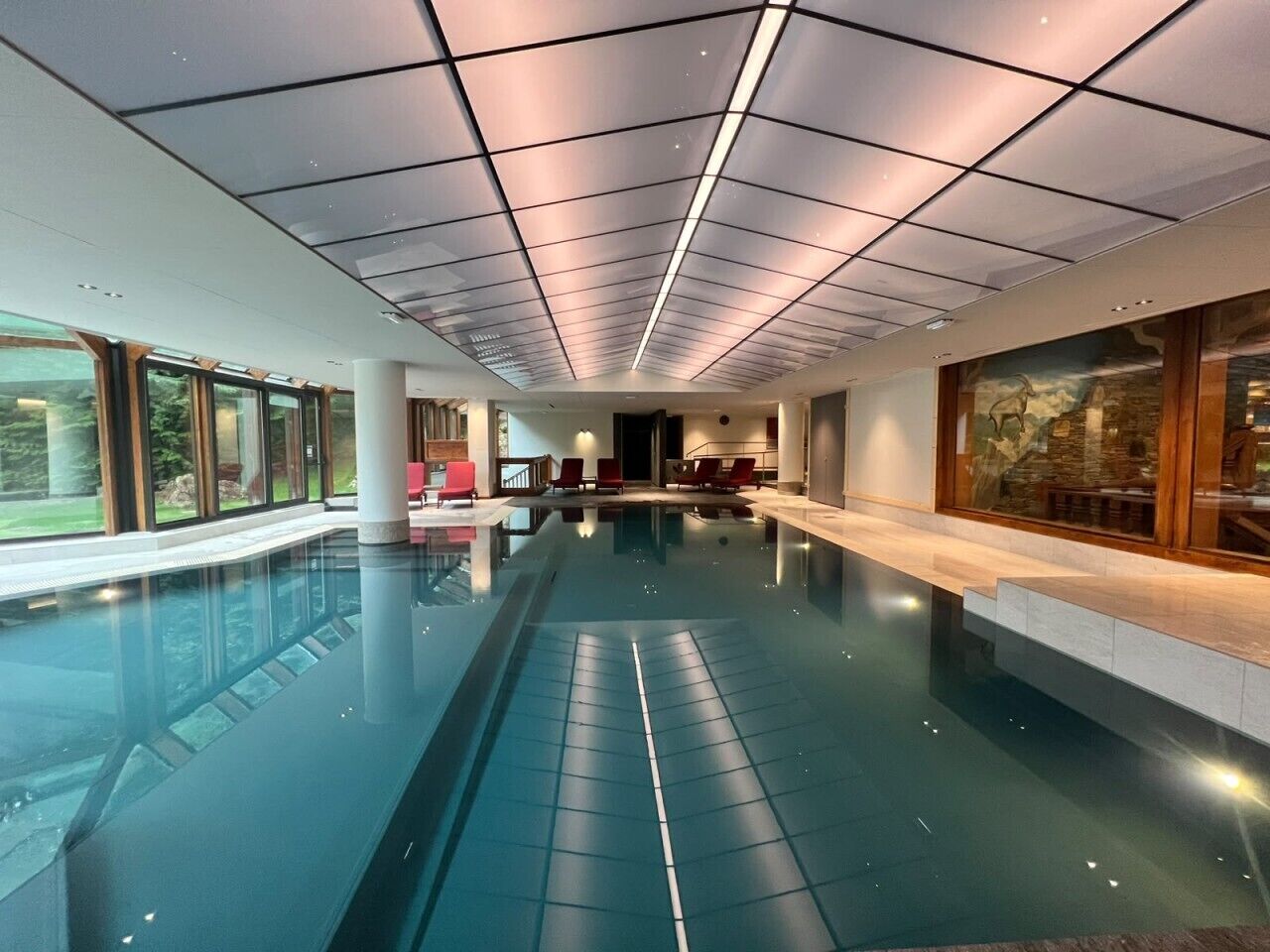 Una amplia piscina interior con paredes de vidrio transparente, techo de azulejos y vistas al exterior.