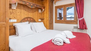 A wooden-paneled room with a bed, a window with curtains, and a wall-mounted light fixture. - Apt central proche des Pistes + Parking & Pool (Chamonix-Mont-Blanc)