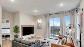 A modern living room with a sofa, a coffee table, a TV, and a fireplace. - Long Term Condo with Pool, Gym, Balcony, Parking   |   Sleeps 6, King Suite + Sleeper Sofa,  Minutes to Downtown & Five Points, Perfect for Long Stays and Remote Work,  24 Hour Hospitality (Nashville)