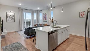 A modern kitchen with a central island, a dining area with a sofa, and a view of the outdoors. - Long Term Condo with Pool, Gym, Balcony, Parking   |   Sleeps 6, King Suite + Sleeper Sofa,  Minutes to Downtown & Five Points, Perfect for Long Stays and Remote Work,  24 Hour Hospitality (Nashville)