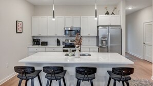 A modern kitchen with white cabinets, stainless steel appliances, and a central island with bar stools. - Long Term Condo with Pool, Gym, Balcony, Parking   |   Sleeps 6, King Suite + Sleeper Sofa,  Minutes to Downtown & Five Points, Perfect for Long Stays and Remote Work,  24 Hour Hospitality (Nashville)