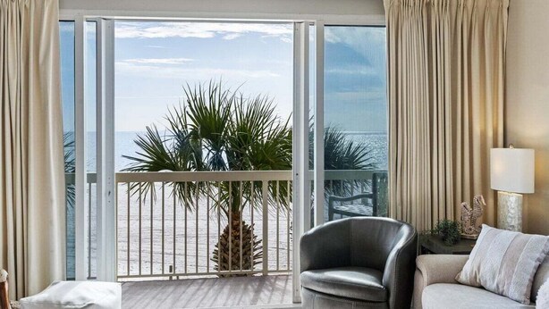 Een hotelkamer met balkon, een bank, een stoel en een lamp.