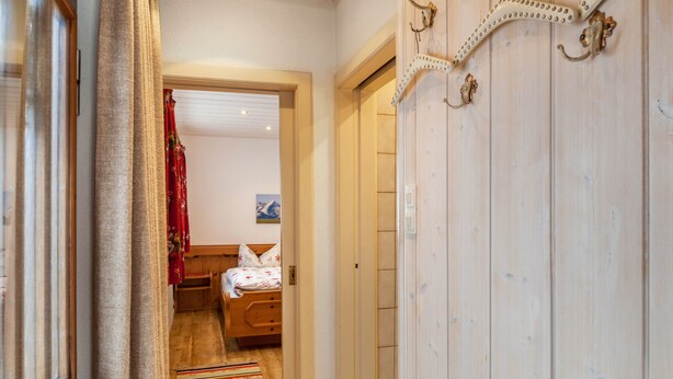 A narrow hallway with a wooden door, a bed with a striped rug, and a red curtain.