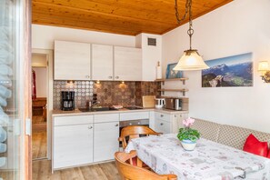 A kitchen with white cabinets, a wooden ceiling, a dining table with a tablecloth, and a sofa with a red pillow.