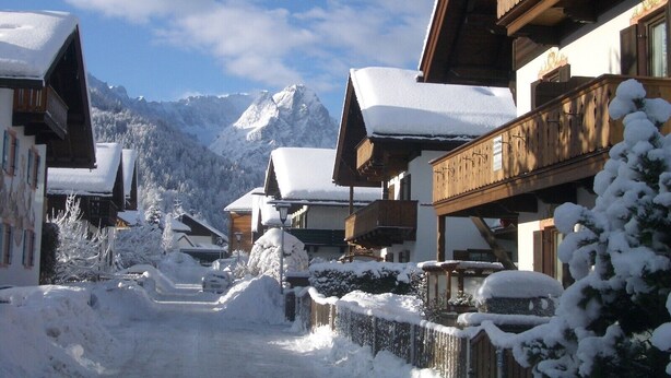 A snow-covered village with wooden buildings, a clear sky, and mountains in the background. - Apartment 'Wank' with Mountain View, Balcony and Wi-Fi (Garmisch-Partenkirchen)
