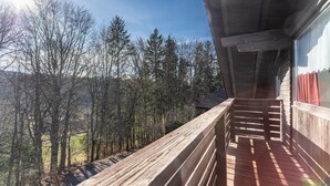Ein Holzbalkon mit Blick auf einen Wald und eine ferne Landschaft.