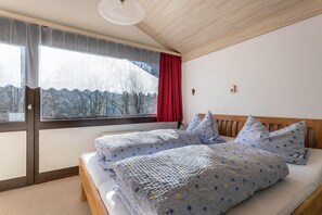 Una camera da letto con una grande finestra, un letto con lenzuola a motivi floreali e un soffitto in legno.