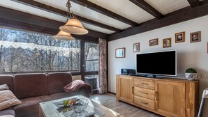 Ein modernes Wohnzimmer mit einer Couch, einem Holzschrank, einem Fernseher und großen Fenstern.