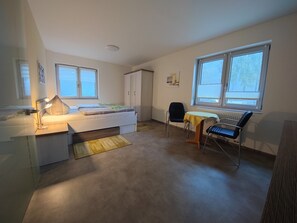 Een slaapkamer met een bed, nachtkastje, lamp, stoel, radiator en ramen.
