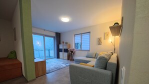 Een woonkamer met een bank, een salontafel, een schuifpui naar een balkon en een wandlamp.