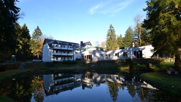 Een gebouw met een spiegelbeeld in een vijver, omgeven door bomen.