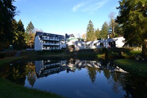 A building with a reflection in a pond, surrounded by trees.