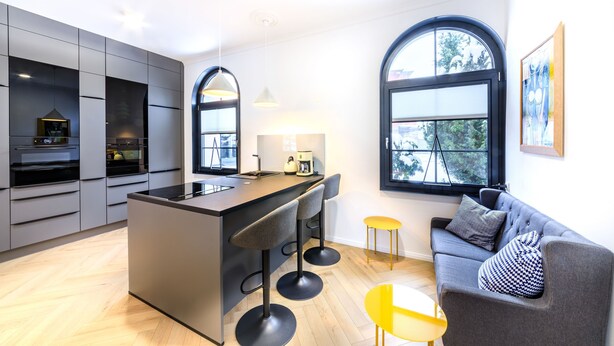 A modern kitchen with a central island, bar stools, a sofa, and a yellow chair. - Holiday Apartment "Schlossplatz Vogtland" with Private Terrace, Private Sauna & Wi-Fi (Auerbach)