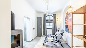 A modern living room with a fireplace, a sofa, a TV, and a bookshelf. - Holiday Apartment "Schlossplatz Vogtland" with Private Terrace, Private Sauna & Wi-Fi (Auerbach)