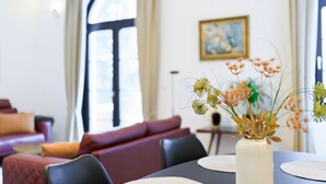 A dining table with placemats, a white vase with dried flowers, and a red sofa in the background. - Holiday Apartment "Schlossplatz Vogtland" with Private Terrace, Private Sauna & Wi-Fi (Auerbach)