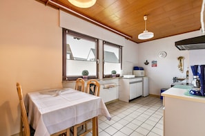 Een compacte keuken met een eethoek, houten plafond en uitzicht door het raam.