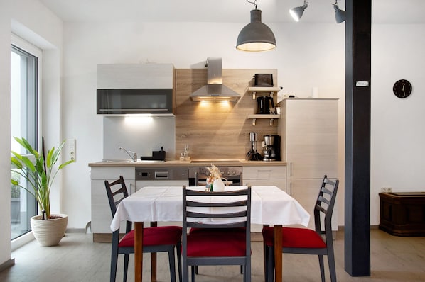 A modern kitchen with a dining area, including a table with chairs, a potted plant, and a clock on the wall.