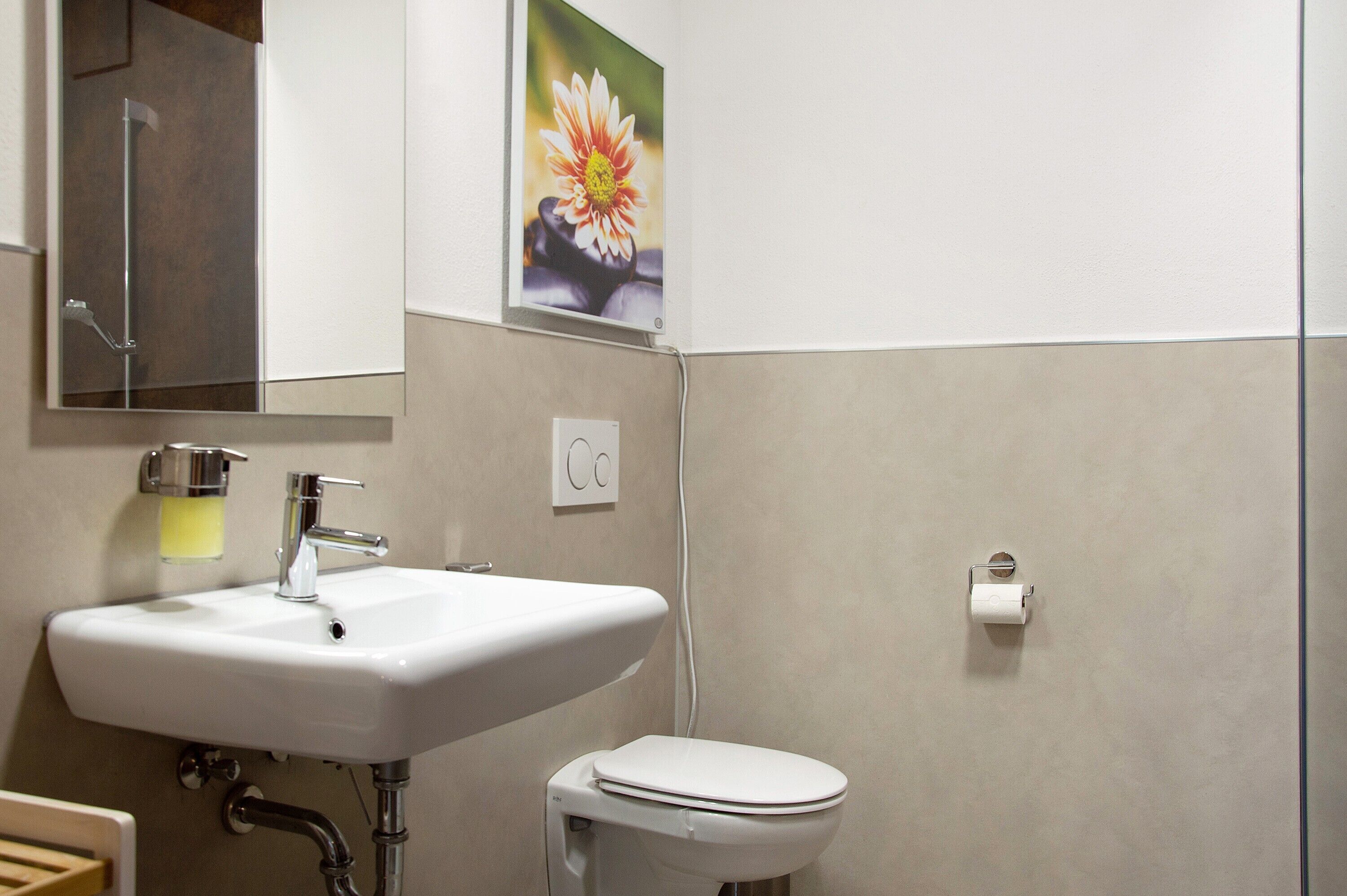 Een badkamer met een wit wastafelmeubel, toilet, spiegel en een bloemenafbeelding aan de muur.