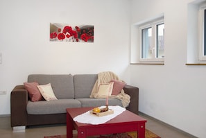 A living room with a grey sofa, a red table, and a painting of red flowers on the wall.
