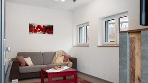 Un salon avec un canapé gris, une table rouge et une œuvre d’art représentant un coquelicot rouge accrochée au mur.