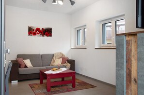 Un salon avec un canapé gris, une table rouge et une œuvre d’art représentant un coquelicot rouge accrochée au mur.