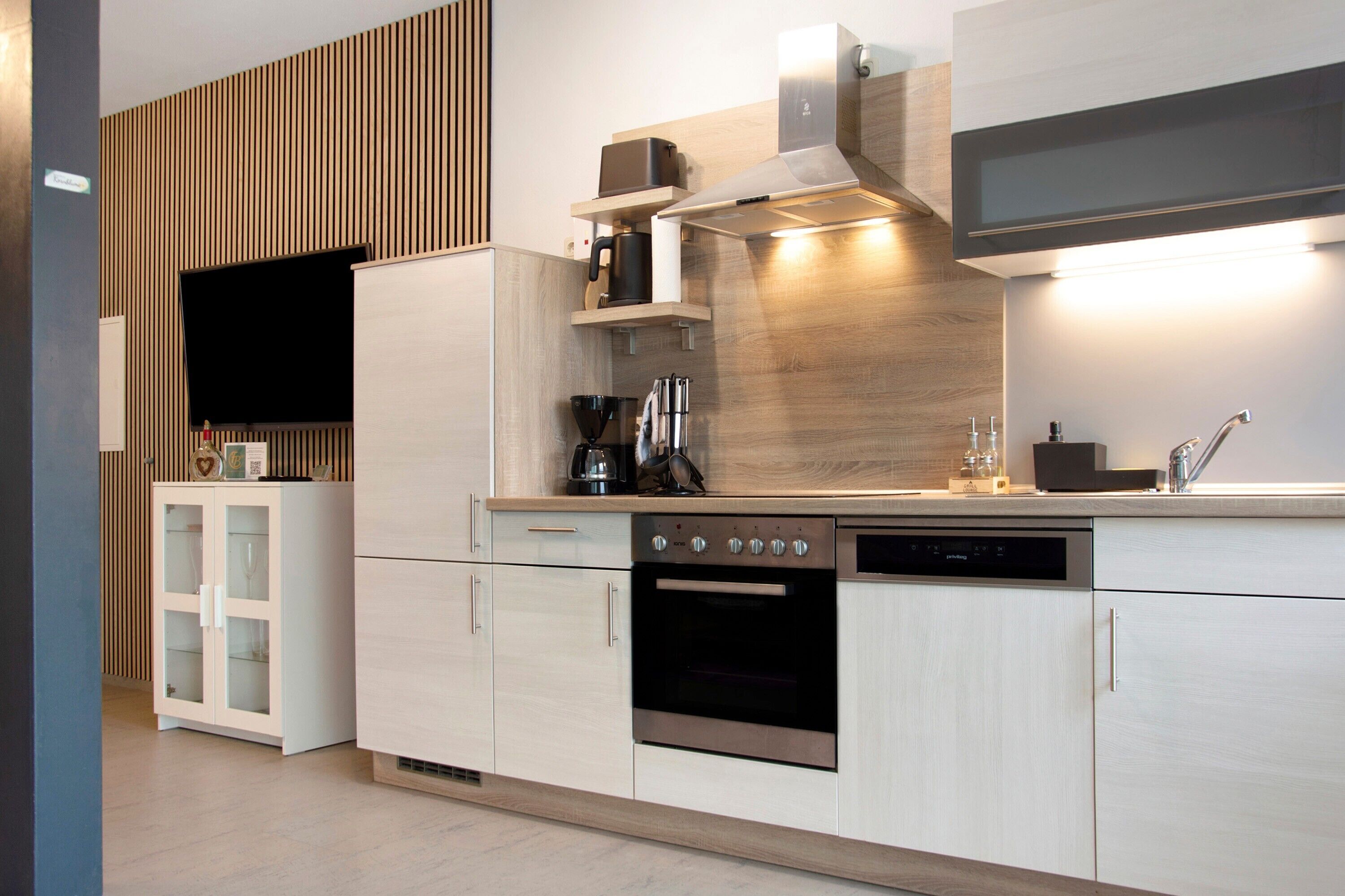 A modern kitchen with built-in appliances, a wooden accent wall, and a flat-screen TV.