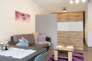 A modern living room with a sofa, a small table, a decorative wall piece, and a wooden partition. - Apartment 'Kornblume' with Private Terrace, Shared Garden and Wi-Fi (Wittighausen)