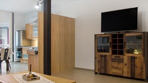 Een moderne woonkamer met een houten kast, een televisie en een eethoek met een tafel en stoelen.