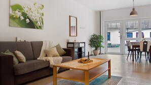 Een woonkamer met een bank, salontafel en een eethoek met stoelen.