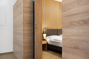 A room with a bed, a nightstand, a lamp, and wooden paneling.