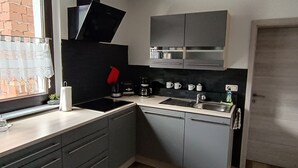 A modern kitchen with grey cabinets, a black range hood, a sink, and a window with lace curtains. - Apartment 'Papperitz' with Mountain View, Private Terrace and Wi-Fi (Uhlstädt-Kirchhasel)
