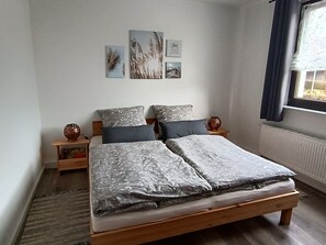 Une chambre à coucher avec un lit en bois, deux tables de chevet, une fenêtre avec des rideaux et des œuvres d’art murales.