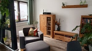 A living room with a sofa, ottoman, wooden cabinet, and a bookshelf. - Apartment 'Papperitz' with Mountain View, Private Terrace and Wi-Fi (Uhlstädt-Kirchhasel)