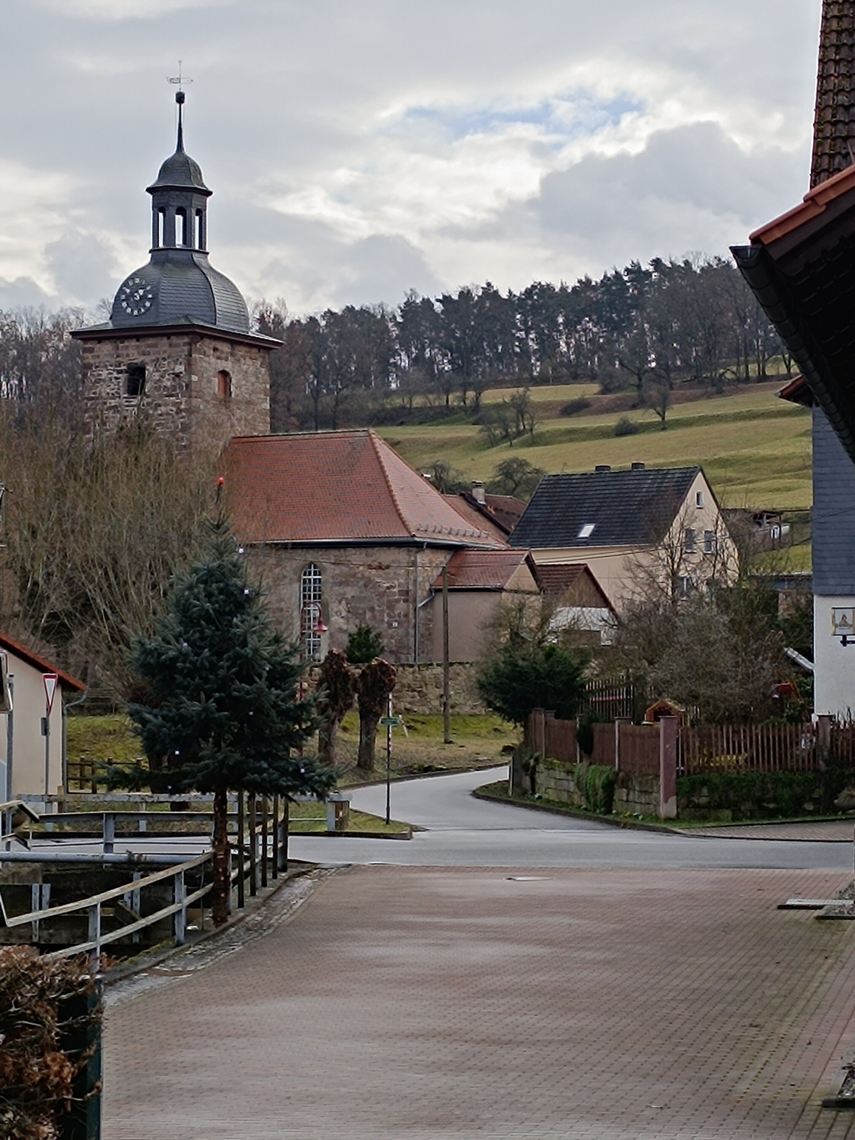 Eine ländliche Straße mit einer Kirche, einem Steinturm und einem asphaltierten Weg.