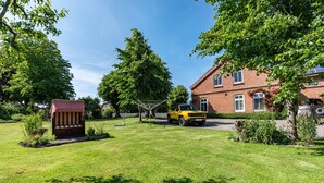 A residential setting with a well-maintained lawn, a yellow vehicle, and a brick house with a visible chimney. - Apartment 'Ferienwohnung Bauernhof Rohde' with Shared Terrace, Private Garden and Wi-Fi (Gremersdorf)