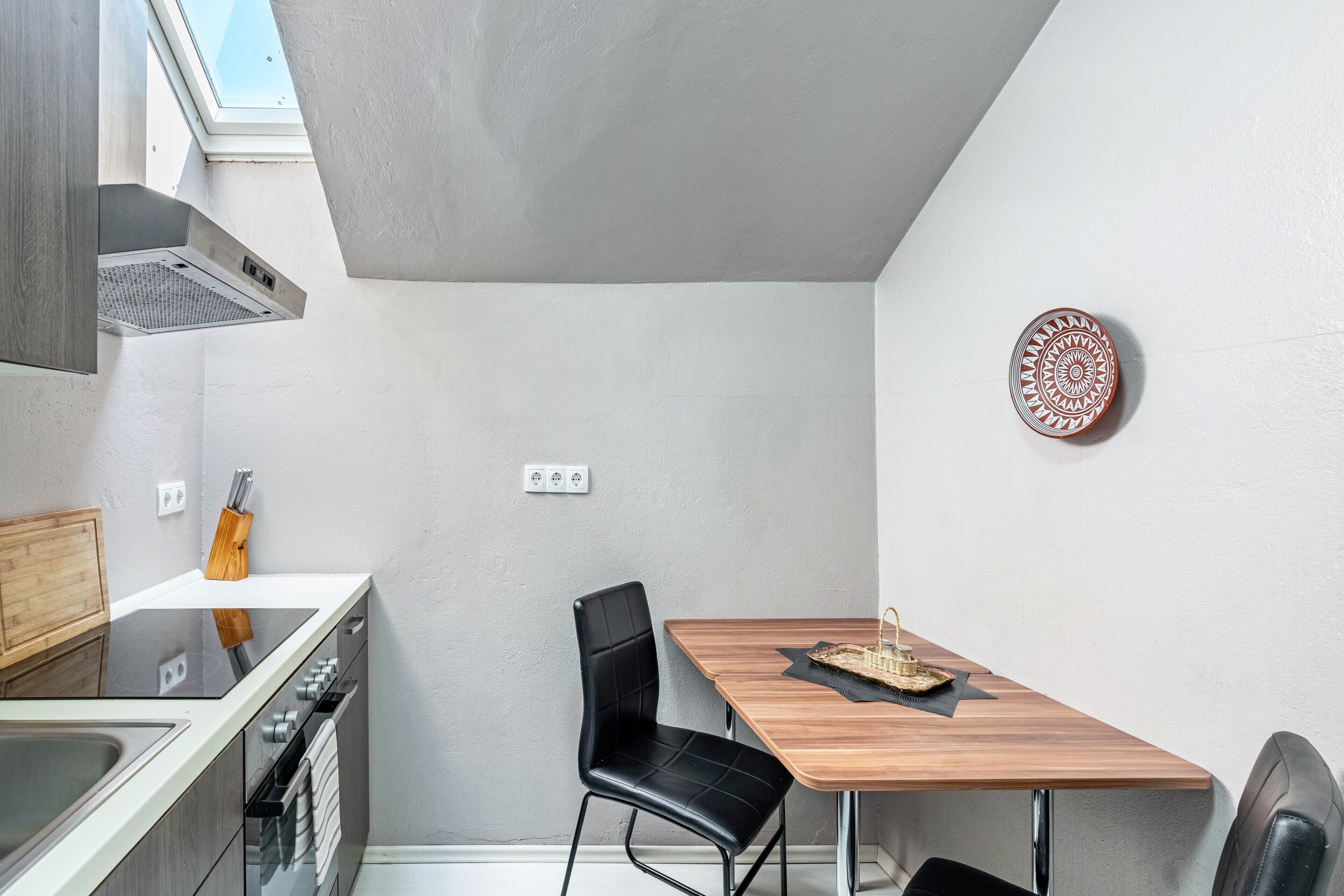 Cocina compacta con estufa, horno y lavamanos, una mesa de comedor con sillas y un tragaluz.