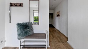 Un hall d’entrée moderne avec un banc, un porte-manteau, un miroir et une vue sur le couloir.