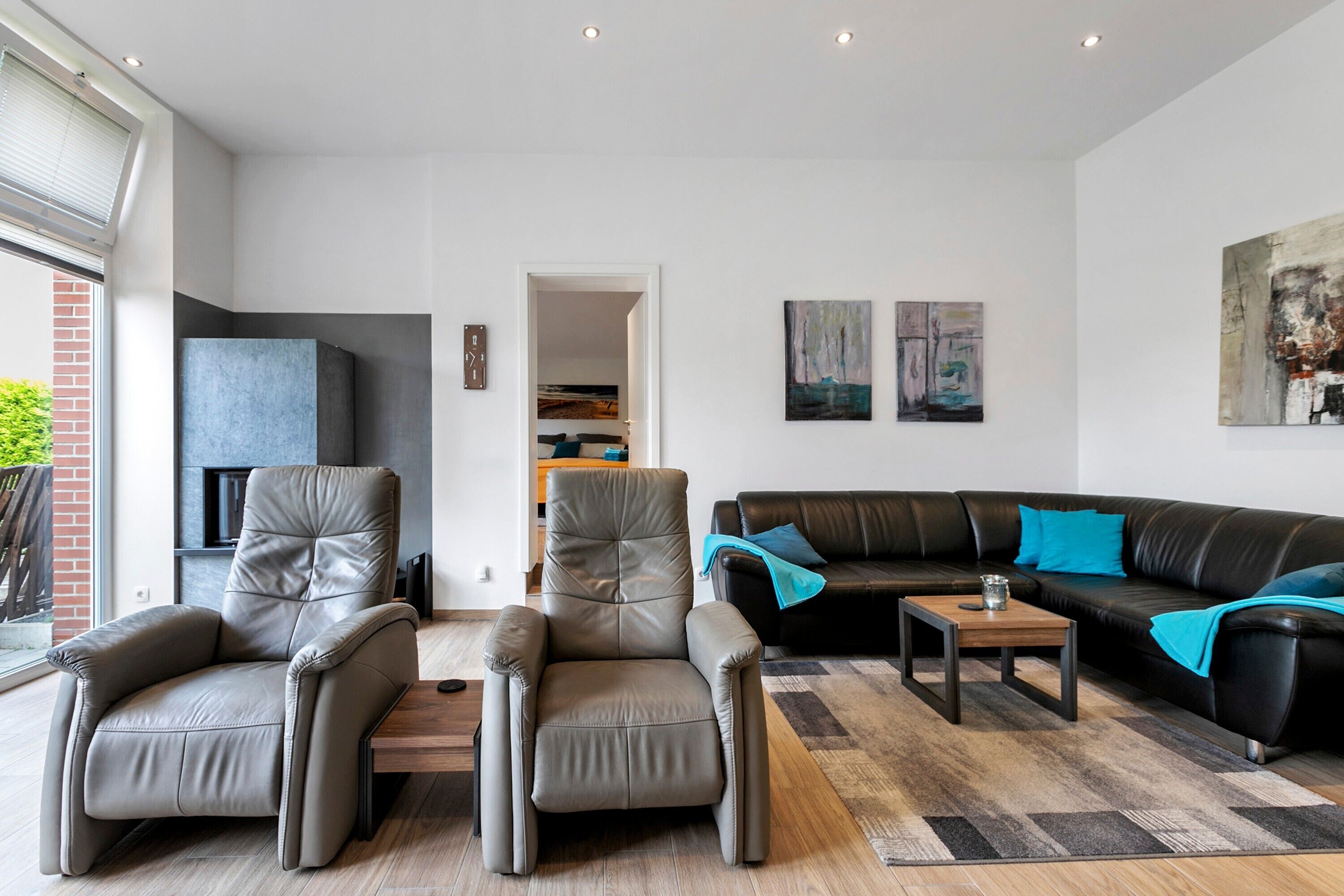 En moderne stue med sofa, to lænestole, sofabord og billeder på væggene.