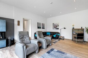 Ein modernes Wohnzimmer mit Ledersofas, einem Holztisch, einem schwarzen Sofa mit blauen Kissen und einem Bücherregal.