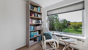 Une pièce comprenant une grande bibliothèque, un fauteuil à bascule, une petite table et une fenêtre donnant sur un paysage verdoyant.