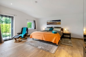 Ein Schlafzimmer mit Bett, Sessel, Fenster und einem Bild an der Wand.