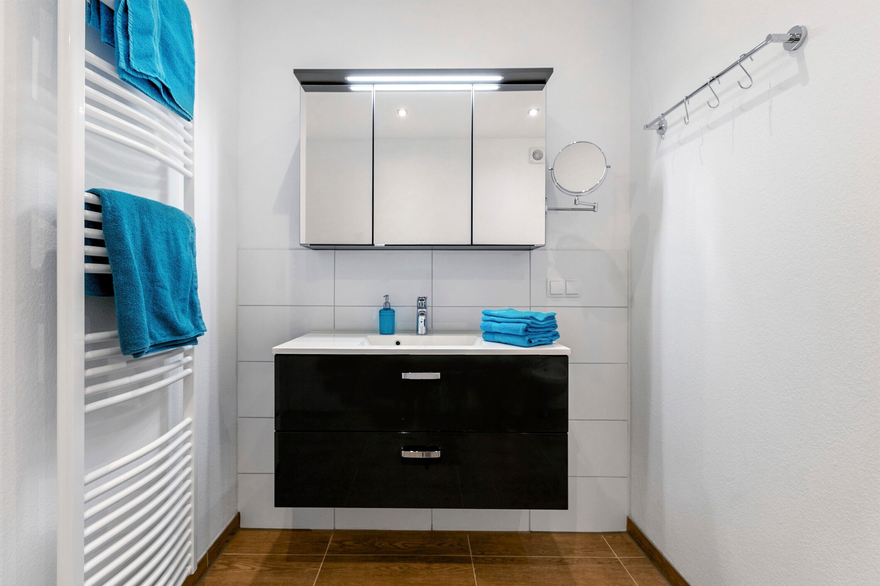 A bathroom with a white sink, black cabinet, and a towel rack.