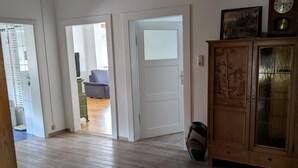 A spacious room with a wooden floor, a chandelier, a cabinet with glass doors, and a door leading to another room.