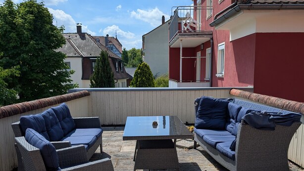 An outdoor patio with wicker furniture, a glass-top table, and a view of neighboring houses.