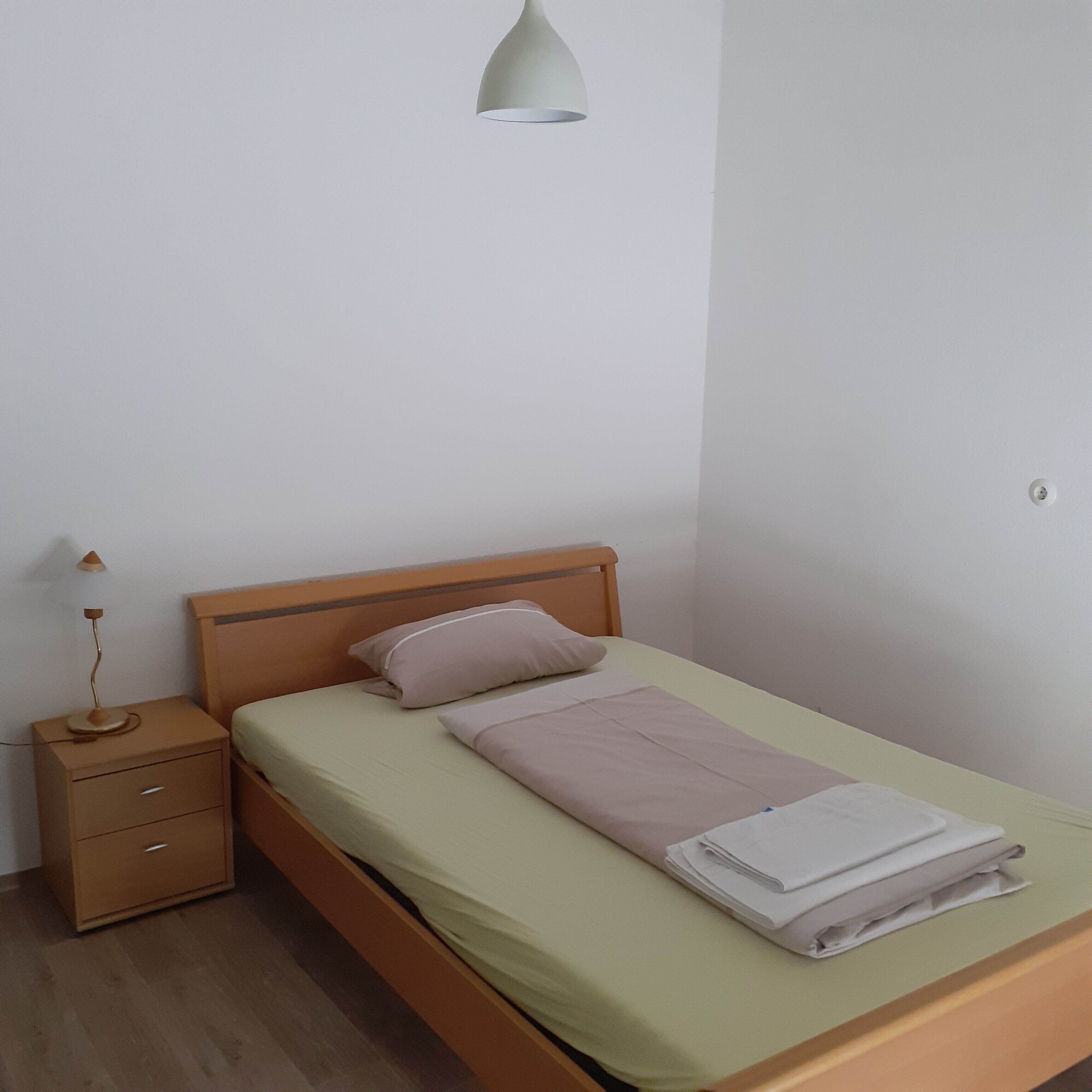 A single bed with a wooden headboard, a bedside table with a lamp, and a wall-mounted light fixture.