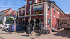A red building with a restaurant sign, a staircase, and parked cars.