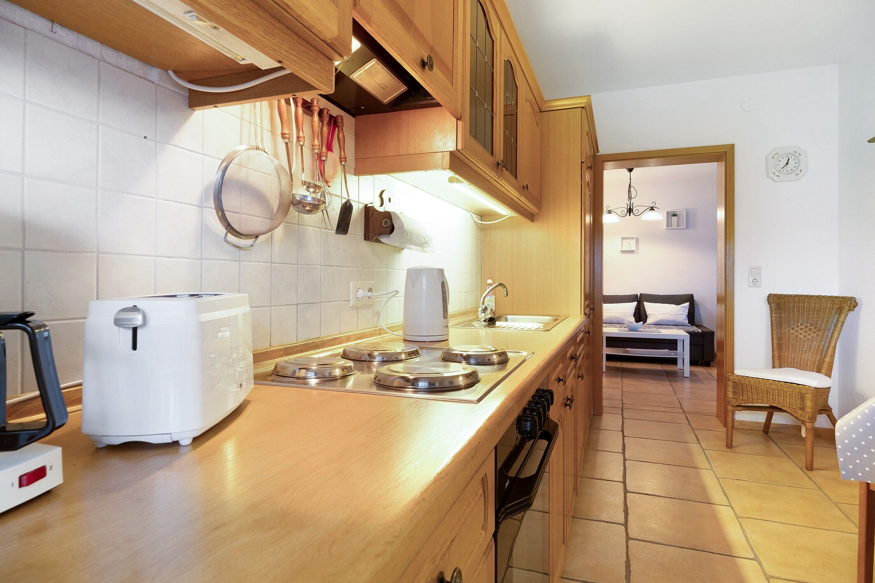 Una cocina con tostadora, hervidor y estufa, armarios de madera y un área de comedor con una silla.
