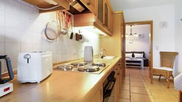 Una cocina con tostadora, hervidor y estufa, armarios de madera y un área de comedor con una silla.